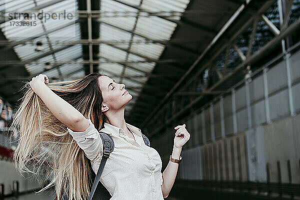 Schöne junge Frau mit geschlossenen Augen und langen blonden Haaren am Bahnhof