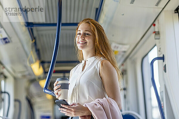 Weibliche Fachkraft hält Mobiltelefon und Einweg-Kaffeebecher im Zug