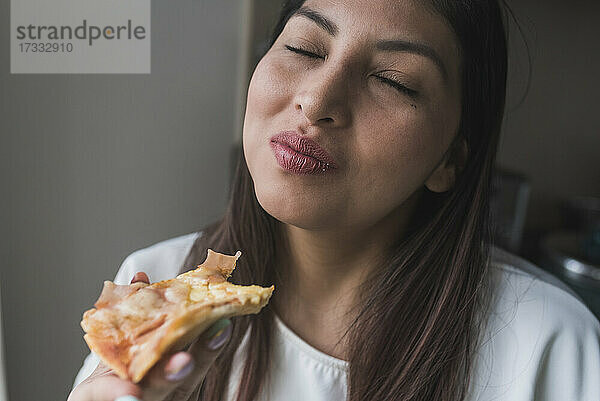Frau mit geschlossenen Augen isst Pizza zu Hause