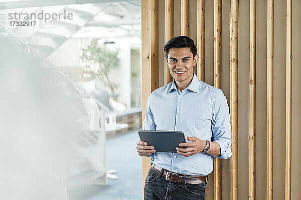 Lächelnder Geschäftsmann mit digitalem Tablet im Büro stehend
