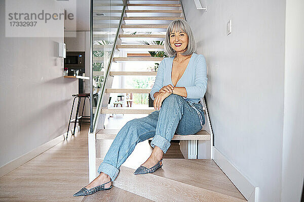 Lächelnde reife Frau sitzt auf der Treppe zu Hause