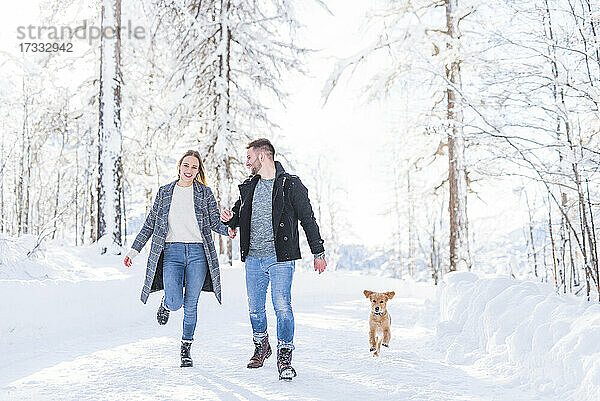 Junges Paar beim Spaziergang mit Hund im Schnee im Urlaub