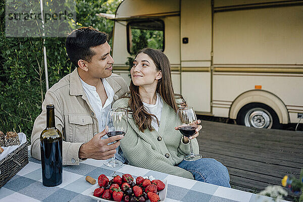 Junges Paar sitzt mit Weingläsern und schaut sich an