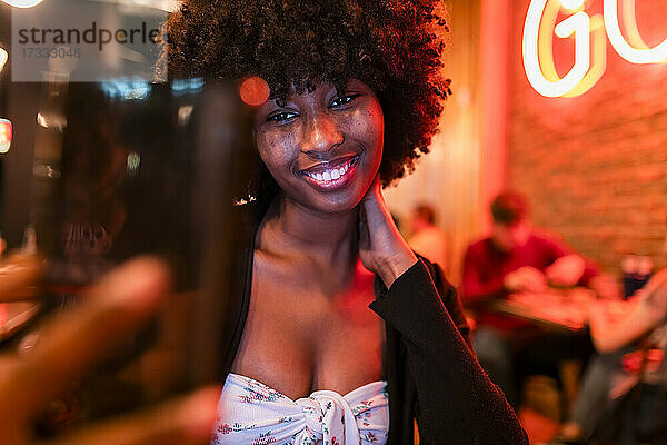 Lächelnde Afro-Frau  die ein Selfie mit ihrem Handy in einer Bar macht