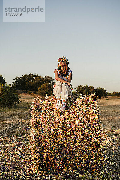 Frau mit geschlossenen Augen auf Strohballen in einem Bauernhof sitzend