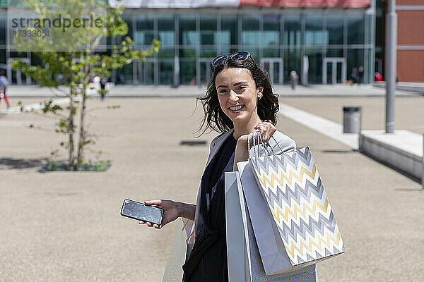 Lächelnde Frau mit Smartphone und Einkaufstüten