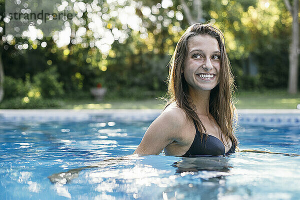 Lächelnde Frau mit braunem Haar im Schwimmbad schaut weg