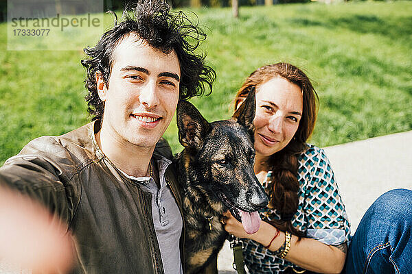 Mann lächelt  während er ein Selfie mit Frau und Haustier macht