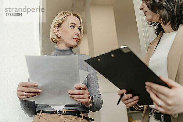 Reife blonde Geschäftsfrau schaut auf weiblichen Profi  der im Büro diskutiert