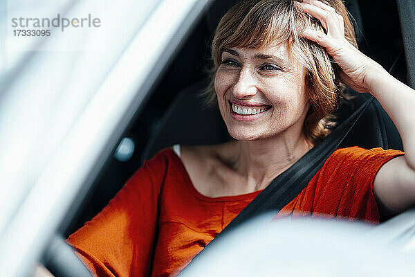 Lächelnde Geschäftsfrau mit Hand im Haar beim Autofahren