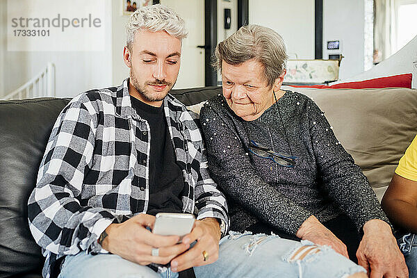 Junger Mann teilt Mobiltelefon mit Großmutter zu Hause
