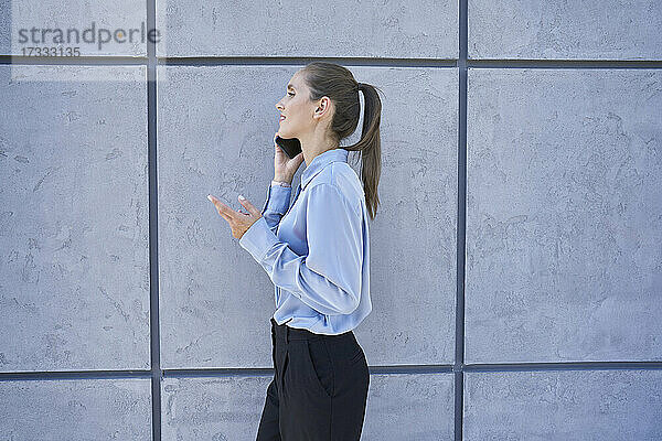 Geschäftsfrau  die mit einem Mobiltelefon telefoniert  während sie an einer Mauer vorbeiläuft