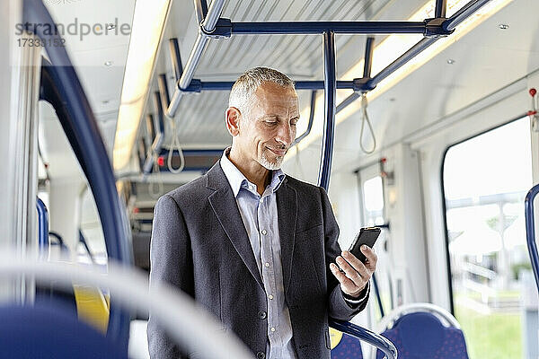 Männlicher Geschäftsmann  der ein Smartphone benutzt  während er in der Straßenbahn steht