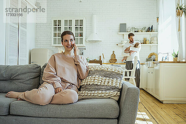 Lächelnde Frau  die mit einem Smartphone spricht  während der Mann seine Tochter zu Hause trägt