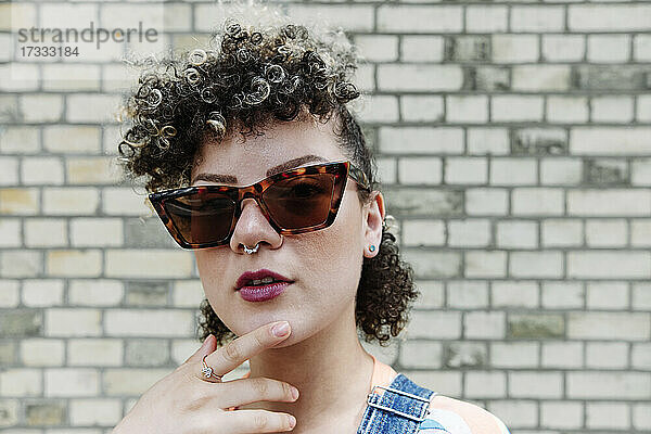 Modische Frau mit Sonnenbrille vor einer Backsteinmauer