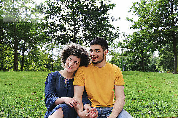 Glückliches junges Paar hält sich an den Händen  während es im Park zusammensitzt