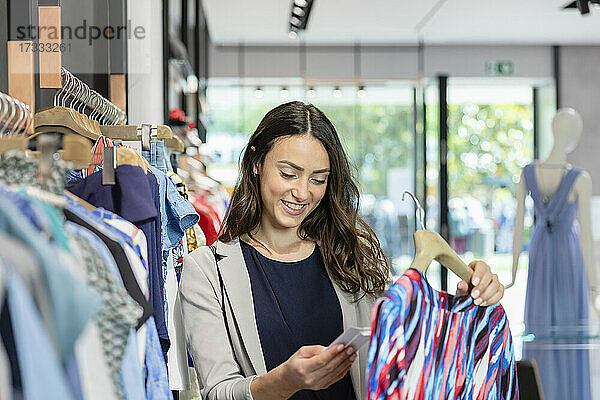 Junge Frau schaut auf das Preisschild und hält ein Kleid in einer Boutique