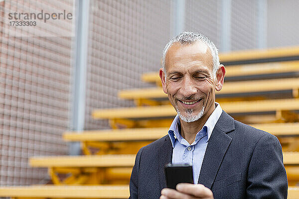 Lächelnder männlicher Fachmann  der ein Smartphone auf einer Treppe benutzt