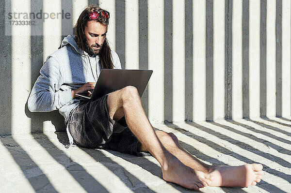 Junger männlicher Freiberufler mit Laptop an einem sonnigen Tag