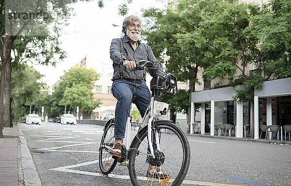 Glücklicher reifer Mann mit Elektrofahrrad auf der Straße in der Stadt