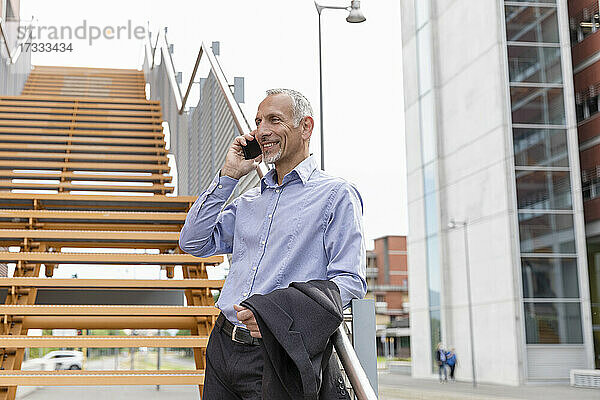 Geschäftsmann  der mit seinem Smartphone spricht  während er sich am Geländer einer Treppe abstützt