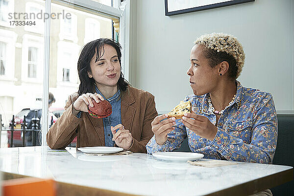 Lesbisches Paar isst Fast Food und sitzt am Tisch in einem Café