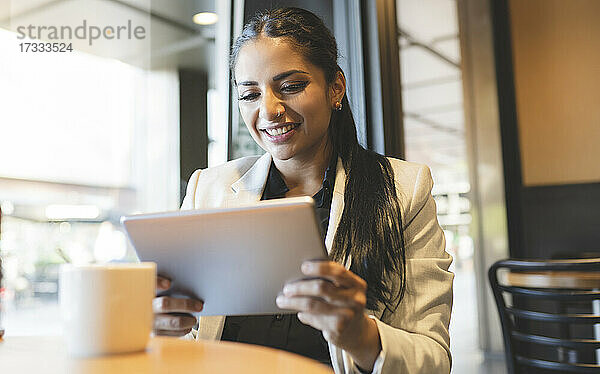 Geschäftsfrau lächelt bei der Nutzung eines digitalen Tablets in einem Café
