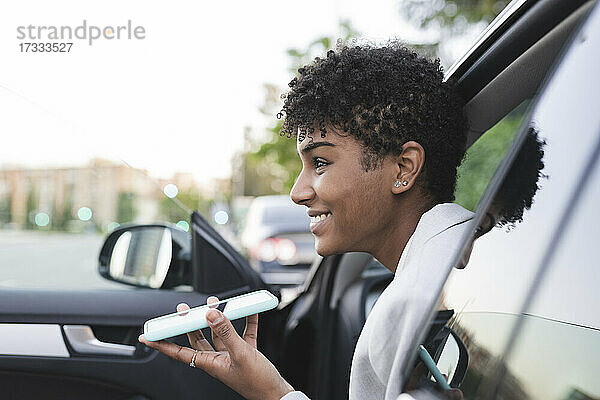 Lächelnde weibliche Fachkraft  die eine Sprachnachricht auf einem Smartphone im Auto sendet