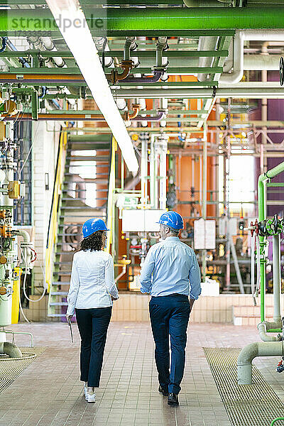 Weiblicher Ingenieur diskutiert mit männlichem Kollegen beim Spaziergang im Kraftwerk