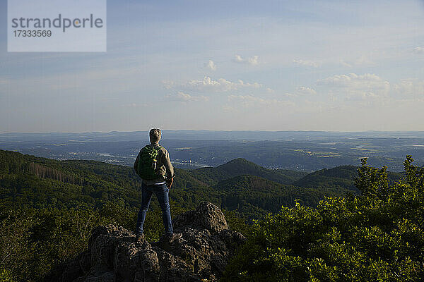 Männlicher Rucksacktourist betrachtet die malerische Landschaft  während er auf dem Gipfel eines Berges steht