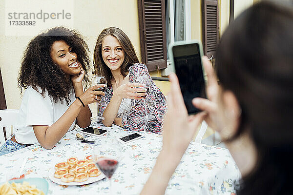 Frau fotografiert Freundinnen auf der Terrasse mit dem Smartphone