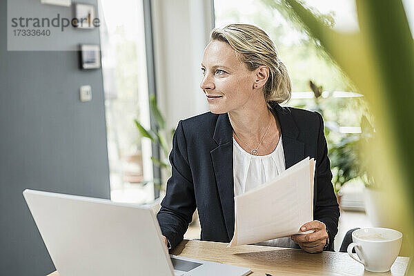 Nachdenkliche Geschäftsfrau mit Dokument und Laptop im Büro