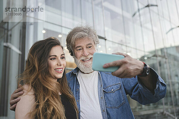 Glücklicher Vater nimmt Selfie mit Tochter durch Smartphone vor Glasgebäude