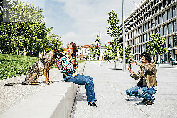 Mann fotografiert Frau mit Hund in der Stadt mit dem Handy