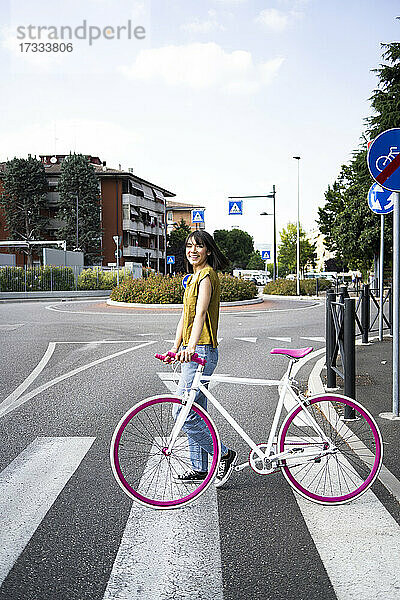 Lächelnde Frau mit Fahrrad auf der Straße stehend