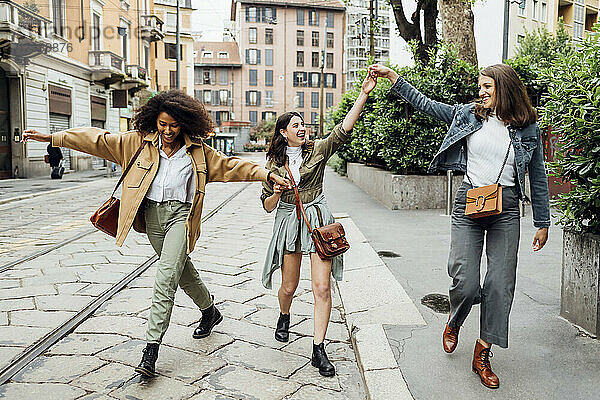 Fröhliche Frauen  die sich an den Händen halten  während sie auf der Straße spazieren gehen