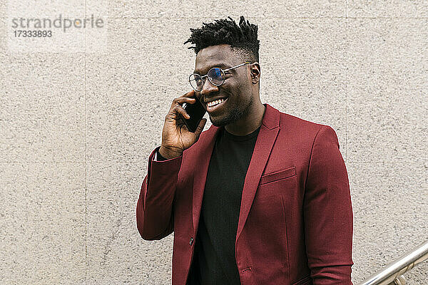 Lächelnder junger Geschäftsmann  der vor einer Wand steht und mit seinem Handy spricht