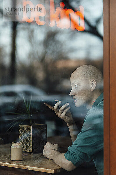 Geschäftsmann  der durch das Fenster eines Cafés mit seinem Mobiltelefon telefoniert