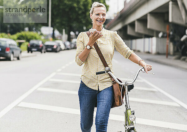 Lächelnde Geschäftsfrau  die mit dem Fahrrad fährt und dabei mit ihrem Smartphone telefoniert