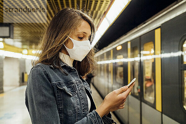 Frau mit Gesichtsmaske  die in der U-Bahn stehend ein Mobiltelefon benutzt