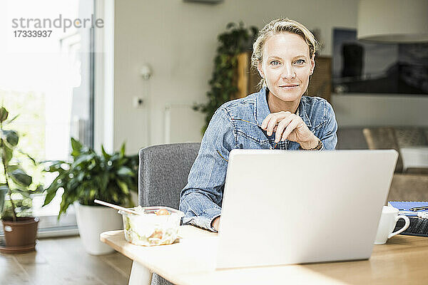 Selbstbewusste Geschäftsfrau mit Laptop  die zu Hause sitzt