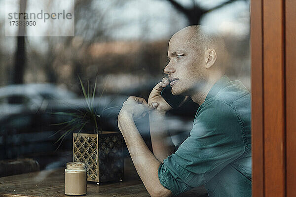 Geschäftsmann schaut durch das Fenster  während er in einem Café mit seinem Handy telefoniert