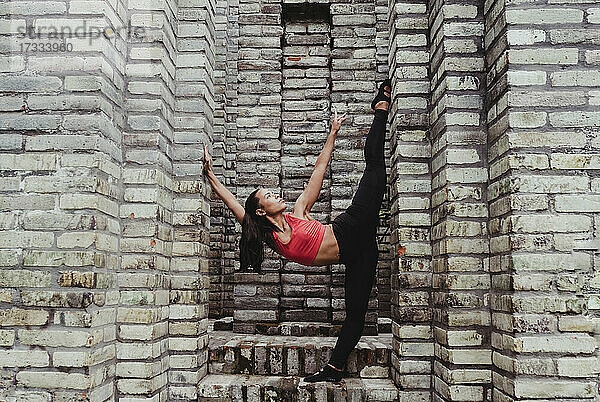 Junge Frau streckt Bein auf Steinmauer