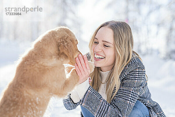 Fröhliche junge Frau streichelt Hund im Winter