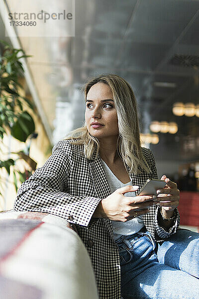 Geschäftsfrau mit Mobiltelefon  die in einem Café sitzt und nachdenkt