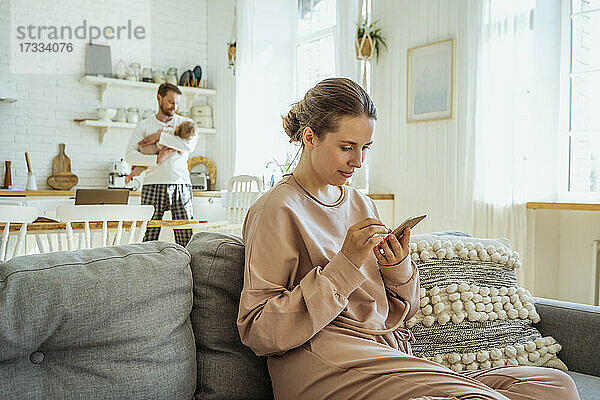 Junge Frau  die ihr Smartphone benutzt  während der Mann seine Tochter in der Küche bei sich hat