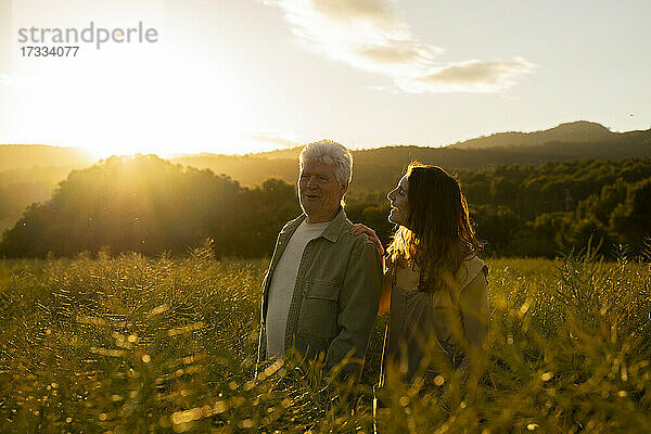 Lächelnde Tochter sieht ihren Vater an  während sie bei Sonnenuntergang auf einem Feld steht