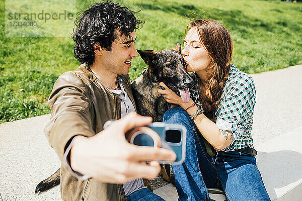 Mann nimmt Selfie durch Smartphone mit Frau küssen Hund während sonnigen Tag