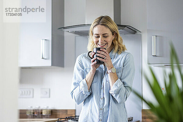 Lächelnde Frau riecht Tee in der Küche zu Hause