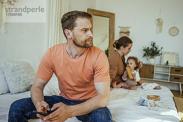 Mann mit Mobiltelefon schaut weg mit Frau und Tochter im Schlafzimmer